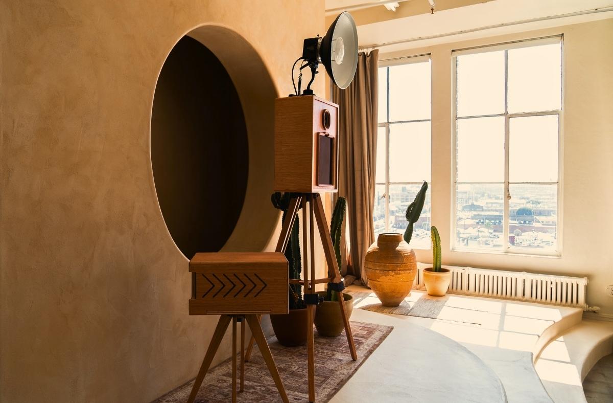 a room with the Glamour Booth, printer shell, tripod, and potted plants