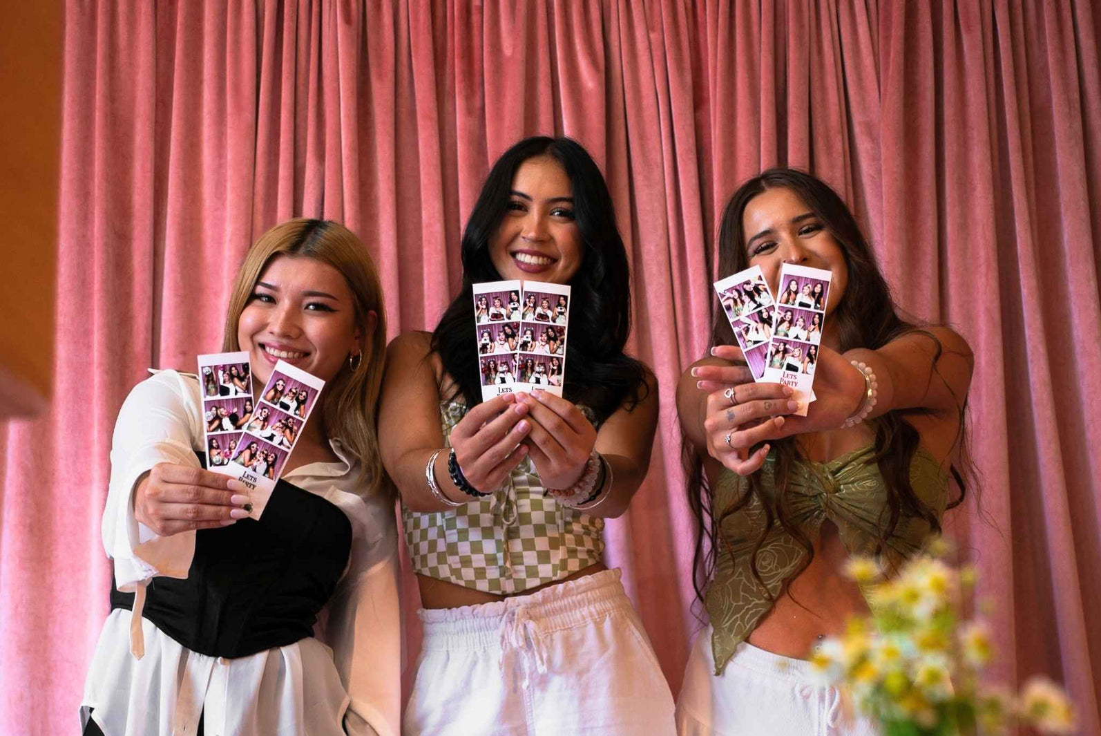 three pretty ladies pose for a picture holding up photo strips from Glamour Booth